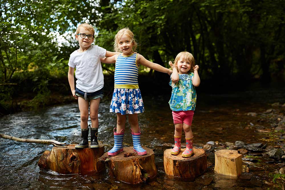 Three young children stood on tree stumps in a stream in Dulverton on Exmoor